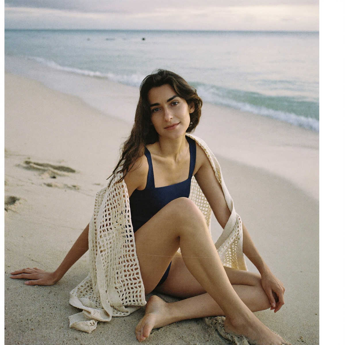 A woman at an Australian beach wearing a wide-strap one-piece swimsuit with an open crochet cover-up